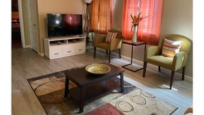 Ein Wohnzimmer mit Fernseher, zwei Sessel, einem Couchtisch und einer Stehlampe.