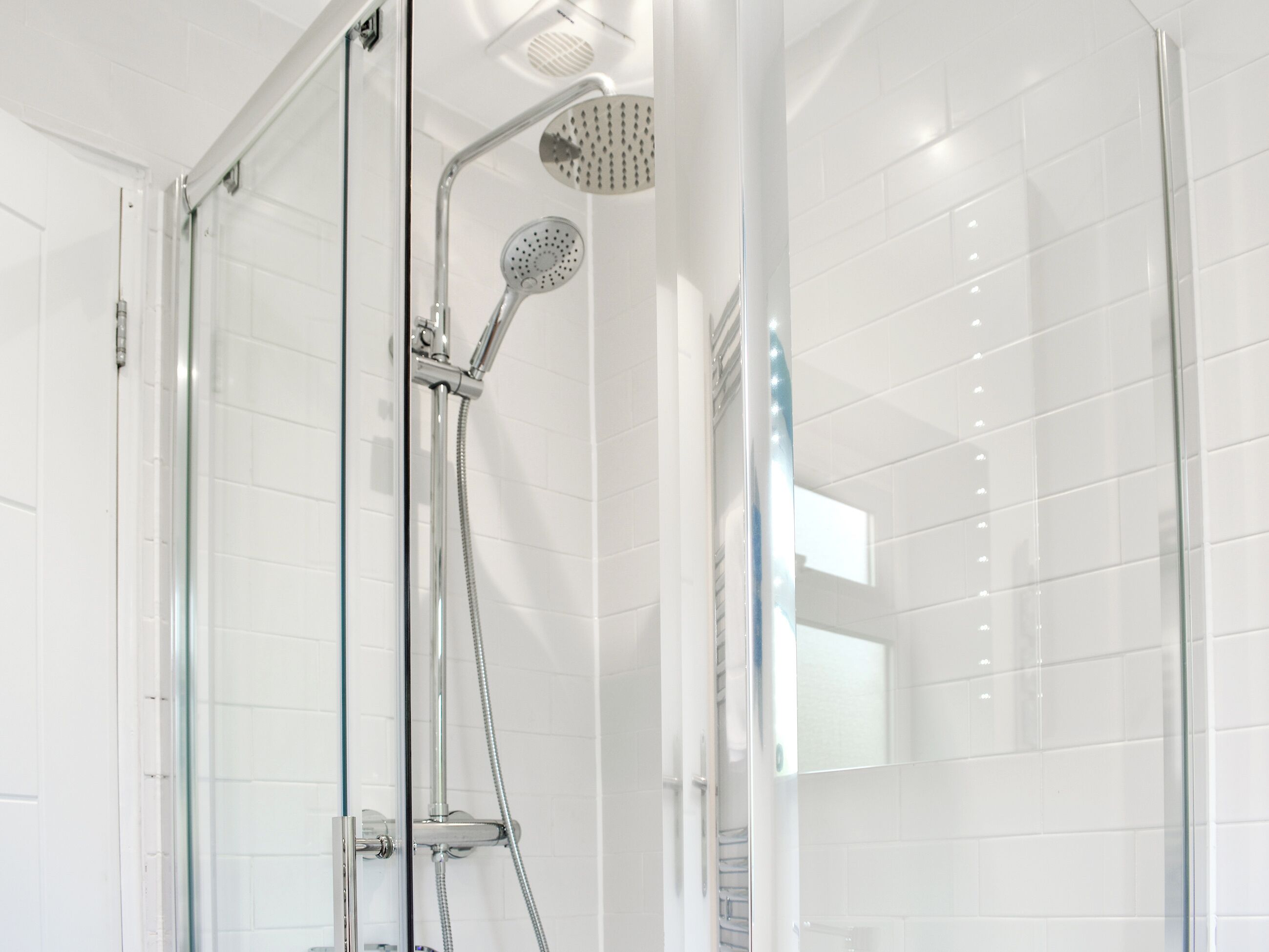A modern shower with a glass door, a handheld showerhead, and a wall-mounted rain showerhead.