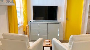 A modern living room with a flat-screen TV on a white cabinet, two white sofas, a small wooden table, and a yellow door. - Happy Hour ACROSS THE STREET FROM THE BEACH (Treasure Island)