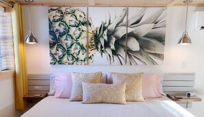 Ein Schlafzimmer mit einem großen Bett, vielen Kissen und einem Wandbild mit tropischen Blättern.