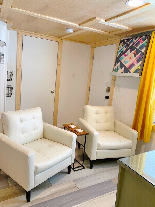 Ein Zimmer mit zwei weißen Ledersesseln, einem kleinen Holztisch und einer Decke mit freiliegenden Holzbalken.