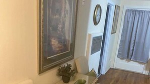 Uma sala de jantar com uma mesa e cadeiras, um quadro na parede, um relógio e uma janela com cortinas.