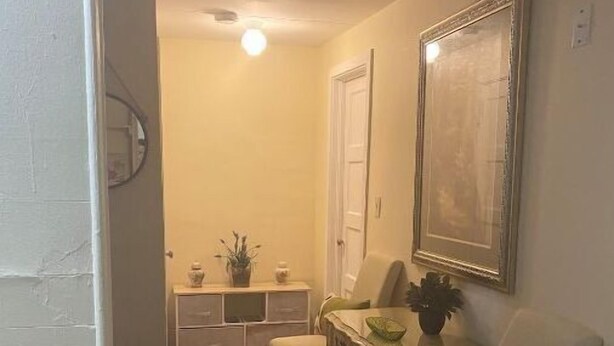 Um corredor com piso de madeira, uma mesa pequena com uma planta, uma cadeira e um espelho na parede.