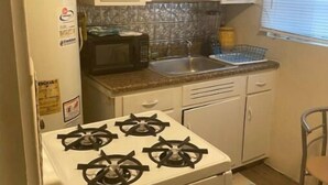 Uma cozinha compacta com armários brancos, fogão a gás, micro-ondas e pia.
