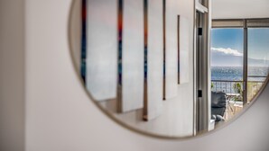 A circular mirror reflecting a room with a balcony, a view of the ocean, and a series of vertical artworks on the wall.