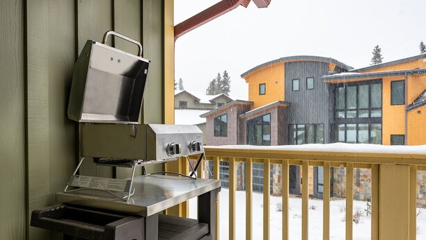 Een balkon met een grill en een piano, met uitzicht op een besneeid gebied en moderne gebouwen.