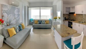 A modern living room with a grey sofa, a kitchen with granite countertops, and a balcony with a railing.