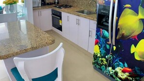 A modern kitchen with white cabinets, a granite countertop, a built-in oven, and a refrigerator with a colorful fish design.