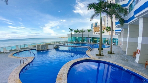 A pool area with multiple swimming pools, palm trees, and a view of the ocean.