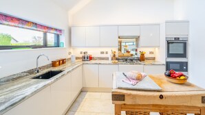 A modern kitchen with white cabinets, a granite countertop, a wooden table, and a fruit bowl.