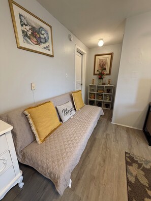 Una habitación con un sofá beige, un aparador blanco, un estante pequeño con adornos y un cuadro en la pared.