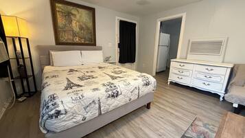 A bedroom with a bed, bedside table, lamp, dresser, and a painting on the wall.
