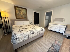 Un dormitorio con cama, mesita de noche, lámpara, cómoda y un cuadro en la pared.