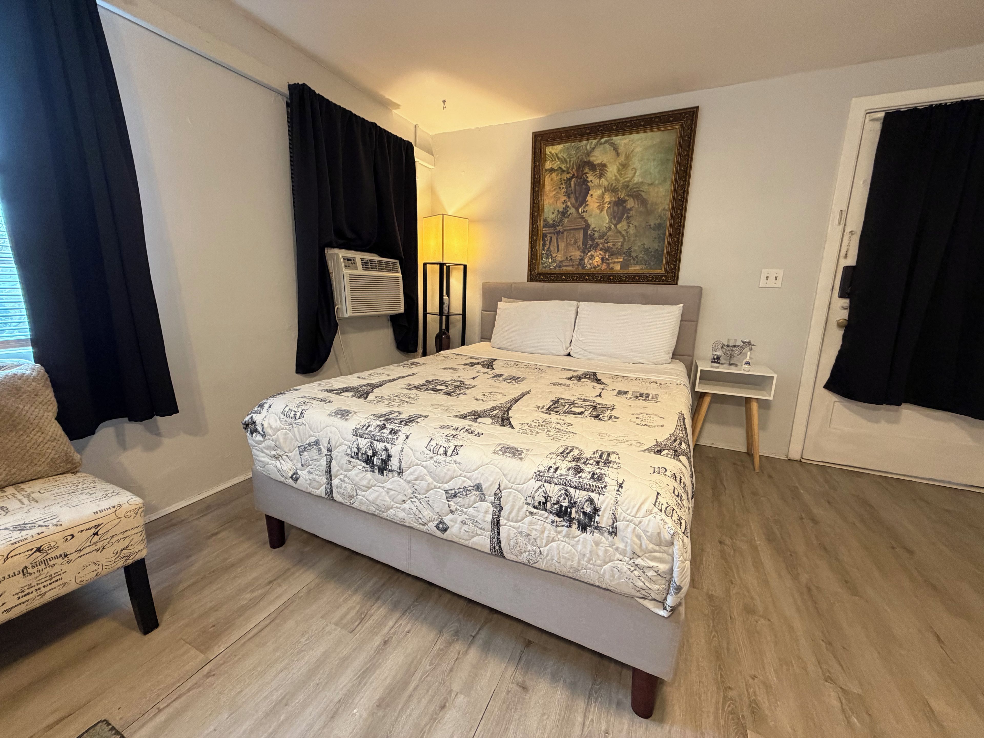 A bedroom with a bed, a chair, a nightstand, a lamp, and a painting on the wall.