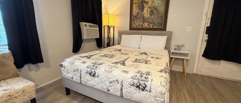 A bedroom with a bed, a chair, a nightstand, a lamp, and a painting on the wall.