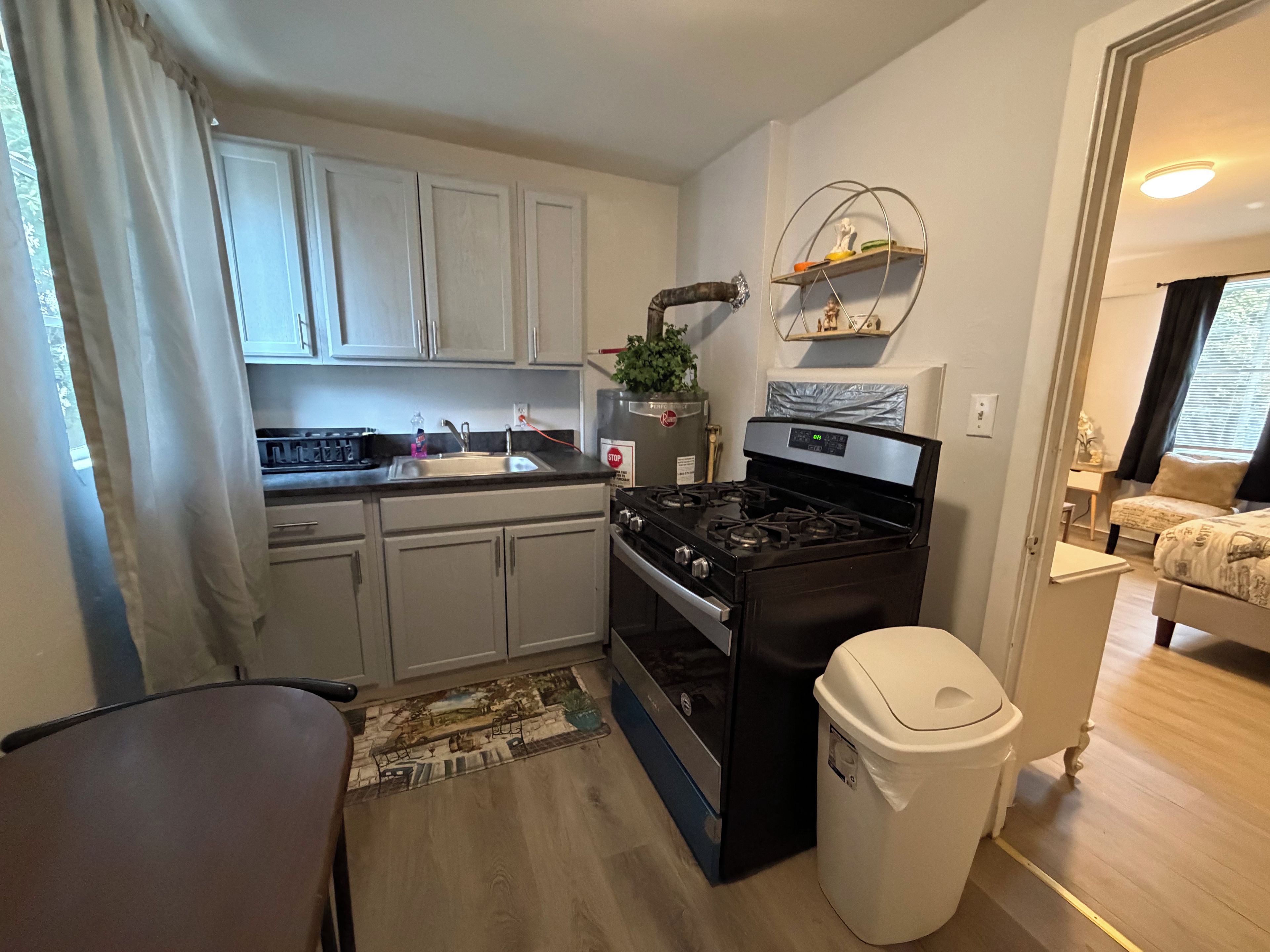 A compact kitchen with white cabinets, a black stove, and a small trash bin.