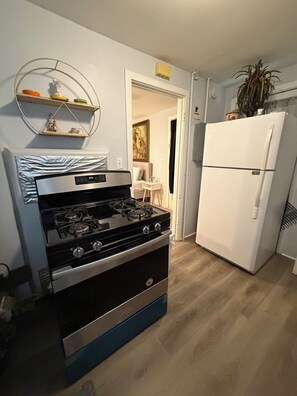 Cocina con estufa a gas, refrigerador blanco y un área de comedor visible a través de una puerta abierta.
