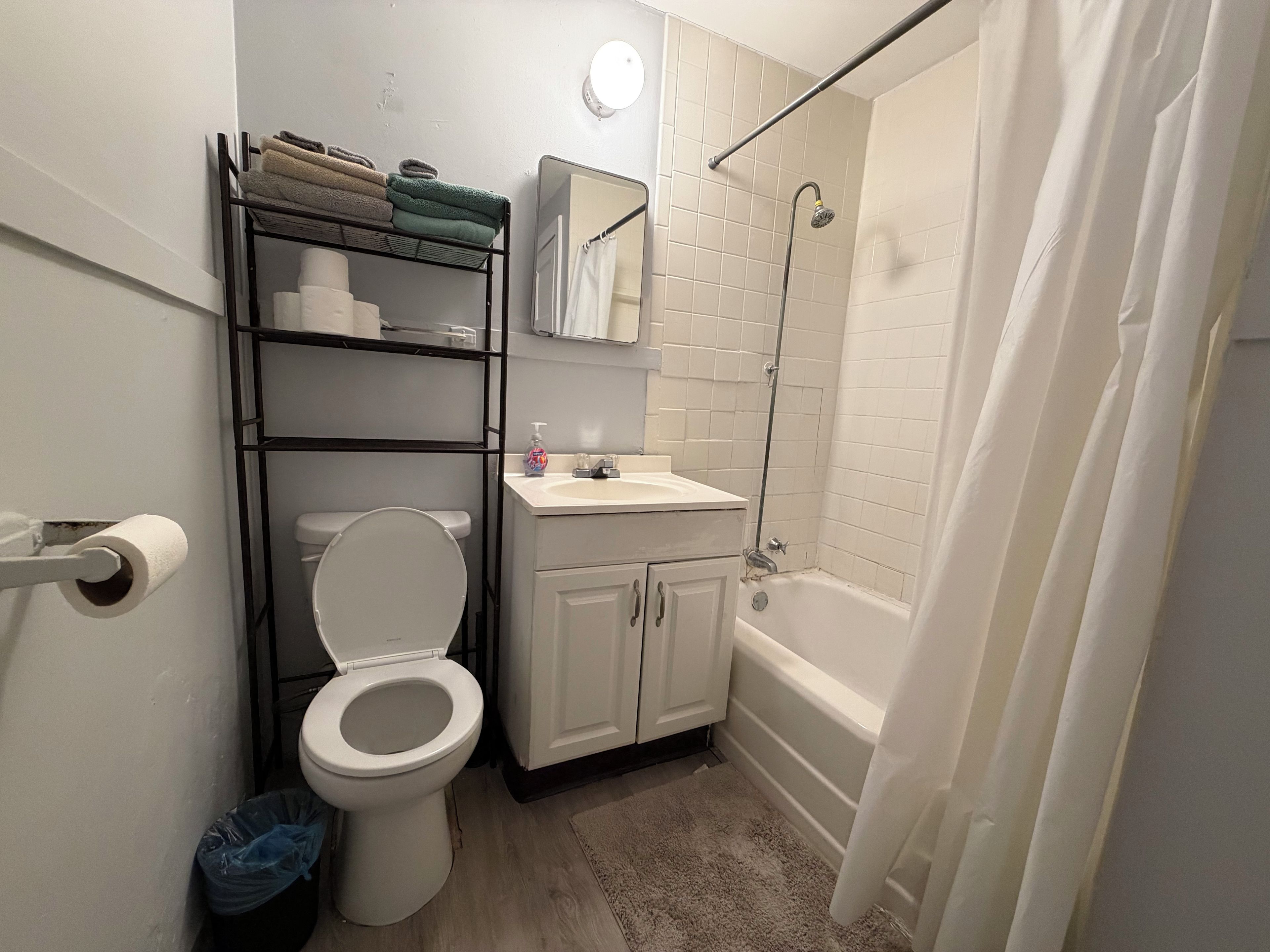A bathroom with a toilet, sink, shower, and a towel rack with folded towels.