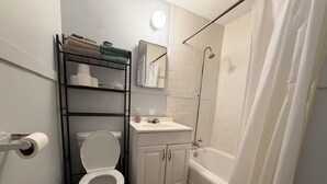 Un baño con inodoro, lavamanos, ducha y un perchero con toallas dobladas.