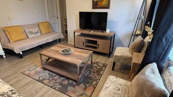 A living room with a sofa, a coffee table, a TV, and a chair with a patterned cushion.