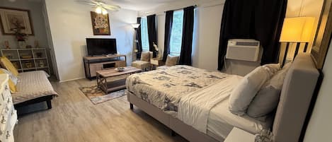 A bedroom with a bed, bedside tables, a TV, a ceiling fan, and a window with curtains.
