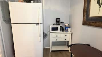 Una cocina compacta equipada con refrigerador, microondas, cafetera y una pequeña mesa.