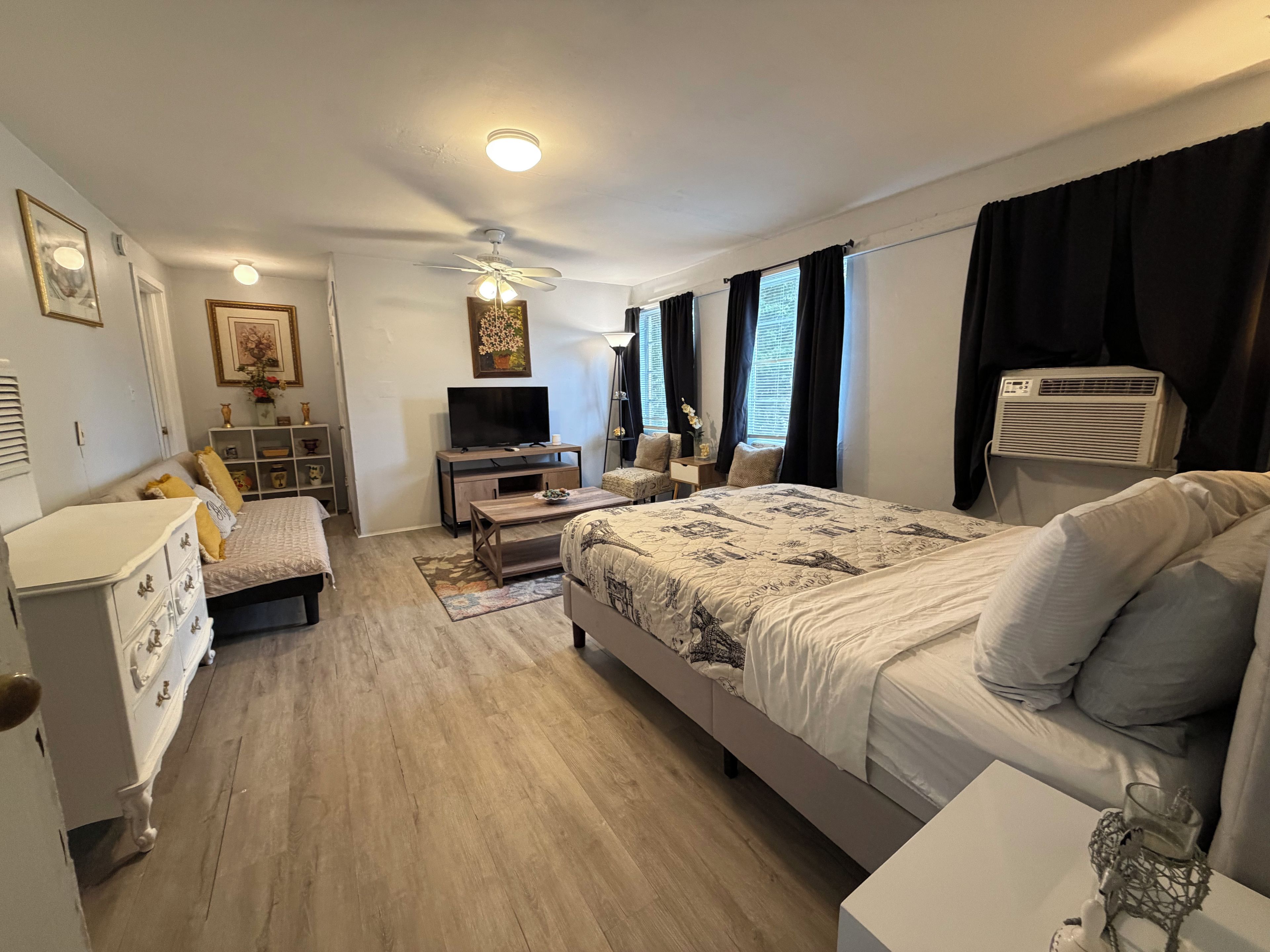 A modern bedroom with a bed, bedside table, dresser, TV, and a ceiling fan.