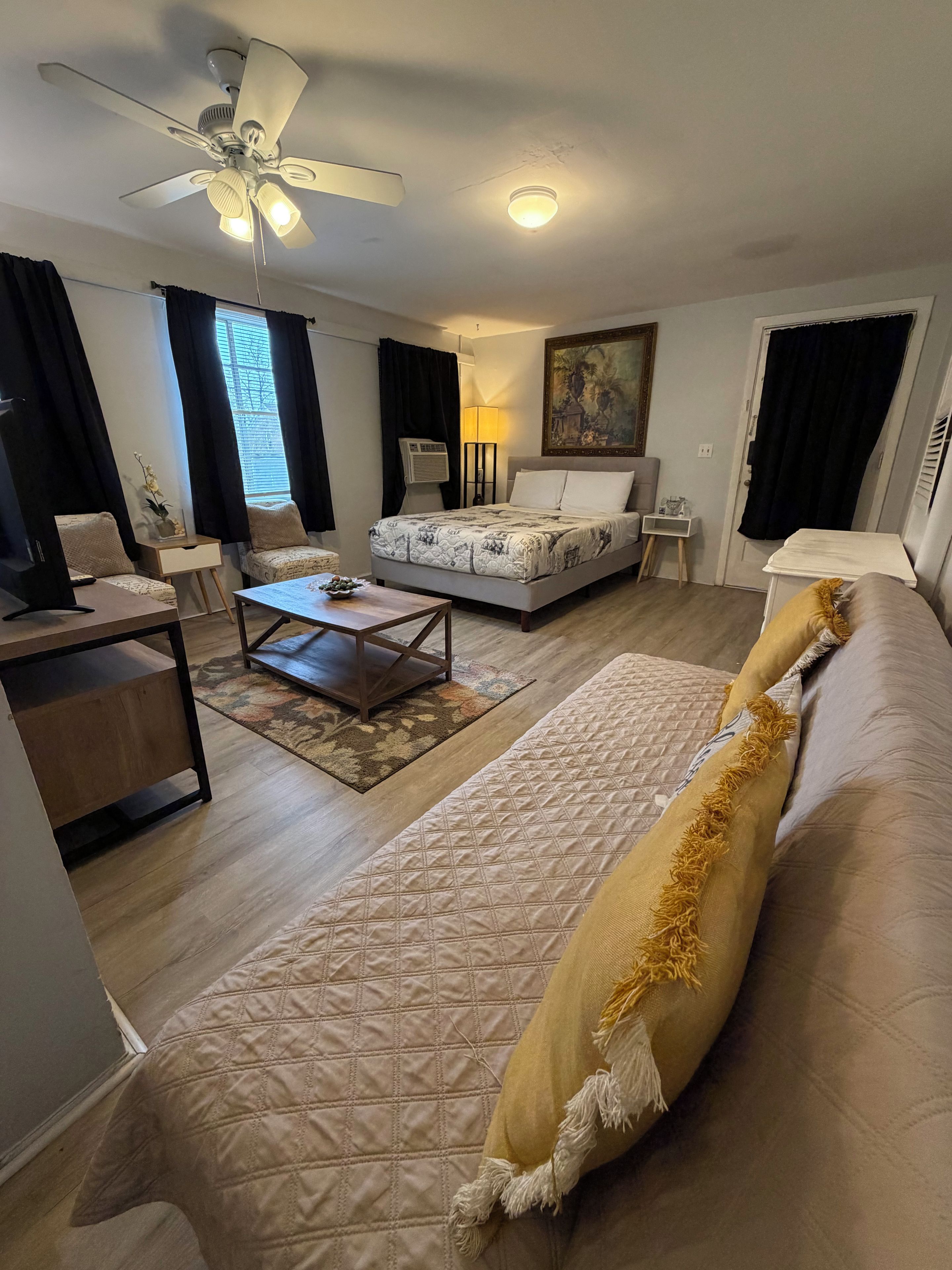 Un salon bien éclairé, équipé d’un lit, d’un canapé, d’une table basse et d’un ventilateur de plafond.