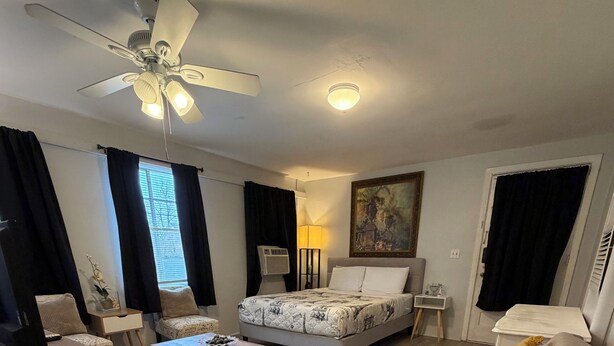 Una sala de estar bien iluminada con una cama, un sofá, una mesa de centro y un ventilador de techo.