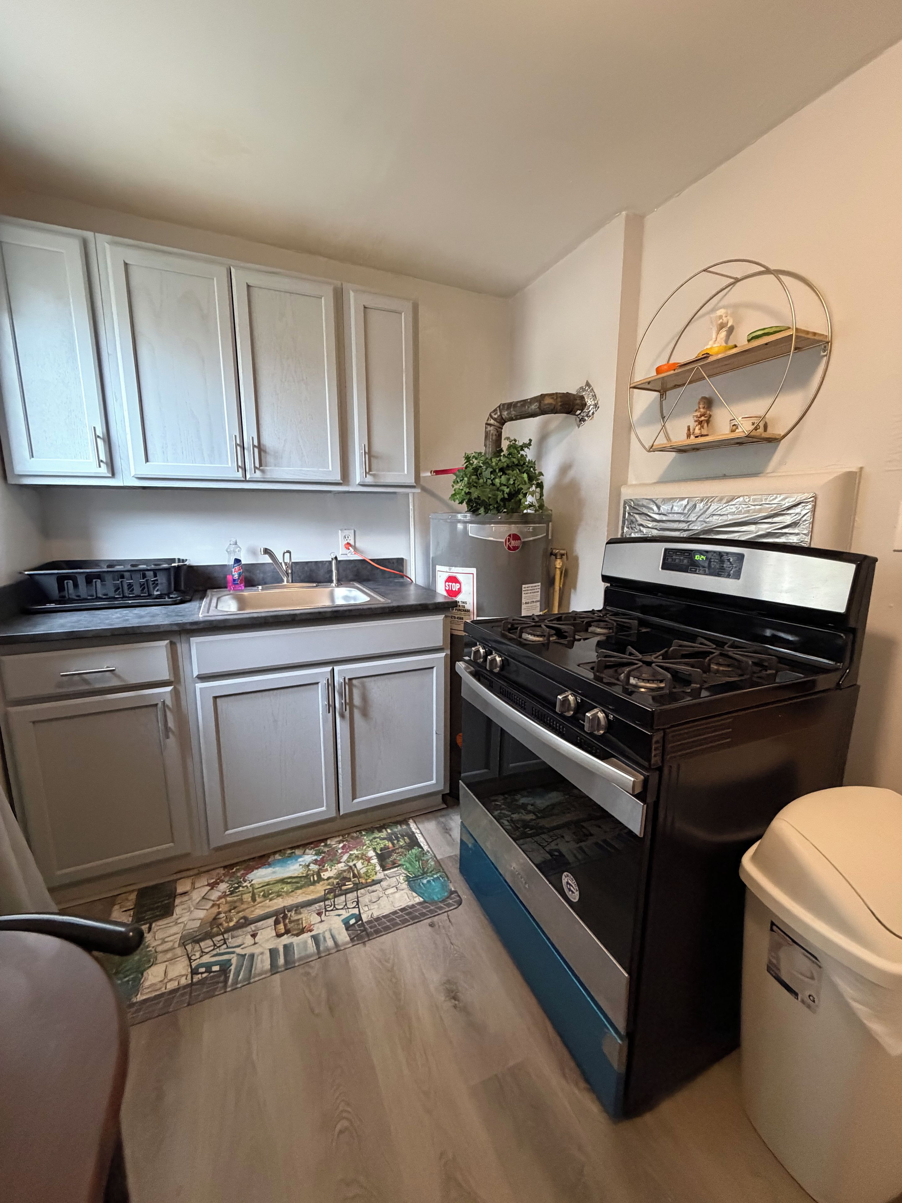 Una cocina con armarios blancos, una estufa de acero inoxidable, un lavabo y un cubo de basura.