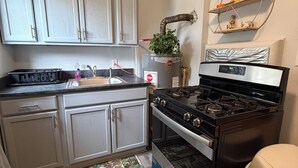Una cocina con armarios blancos, una estufa de acero inoxidable, un lavabo y un cubo de basura.