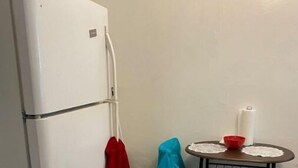 Uma cozinha compacta com geladeira branca, uma mesa redonda pequena com uma vela e um banquinho azul.