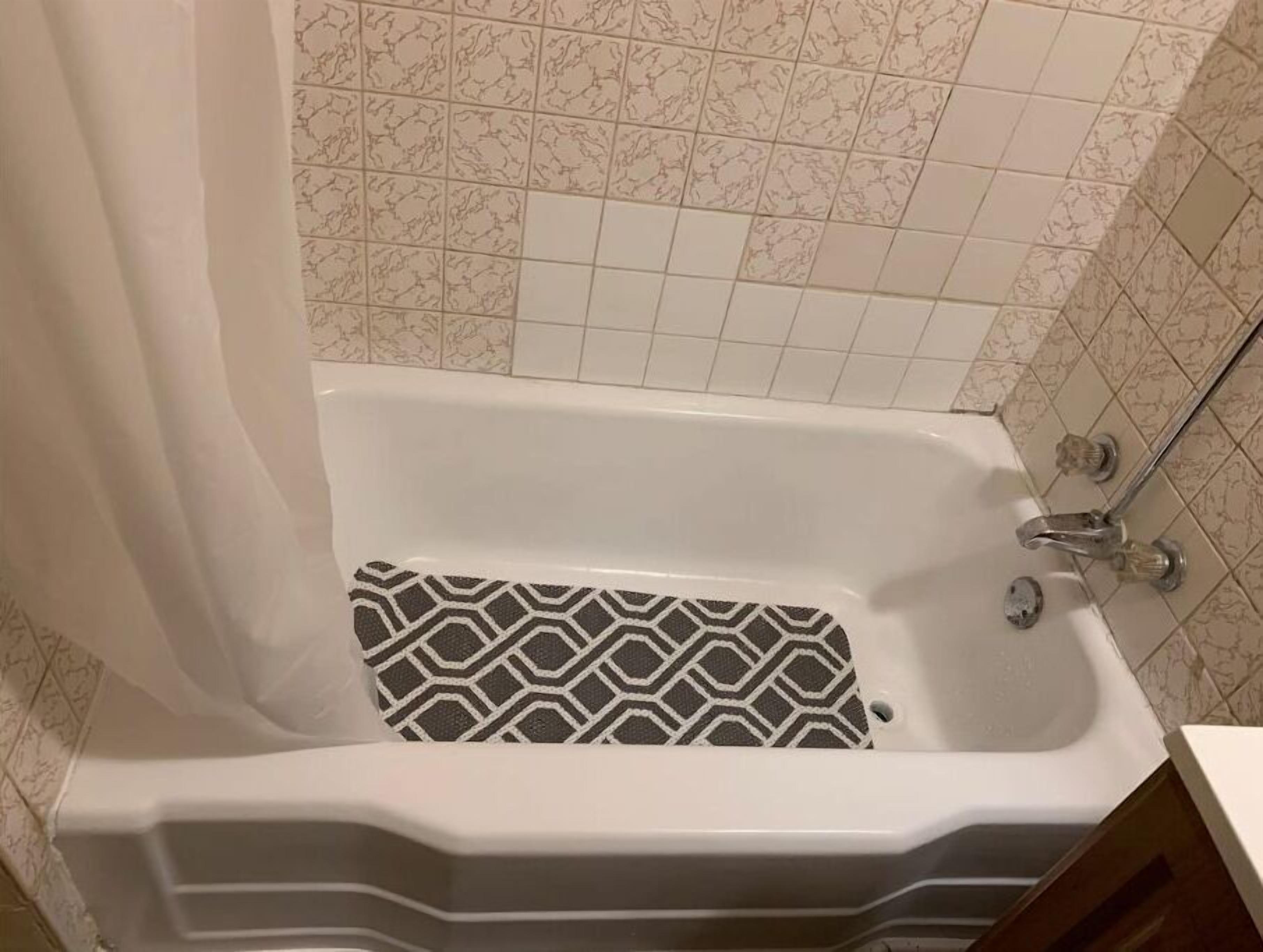 A bathtub with a patterned floor, a shower curtain, and a tiled wall.