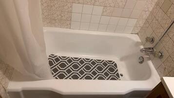 A bathtub with a patterned floor, a shower curtain, and a tiled wall.
