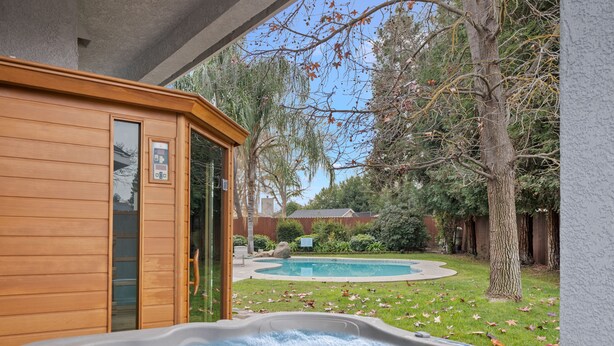 Un jacuzzi con revestimiento de madera y vista a un patio trasero con piscina y árboles.