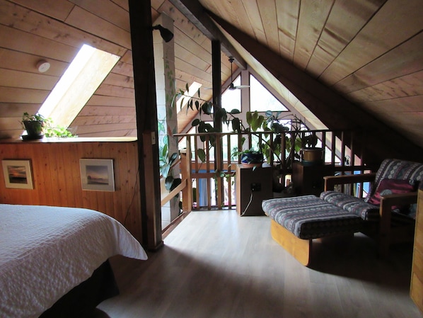 Acogedor dormitorio en el ático con cama, sofá y una escalera que lleva a un balcón.