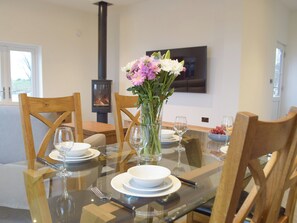 A dining table set with plates, glasses, and cutlery, surrounded by wooden chairs. A vase with flowers is on the table, and a fireplace is visible in the background. - 2 bedroom accommodation in Glandwr, near Narbeth (Glandwr, near Narbeth)