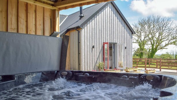 A hot tub with water splashing, a wooden building with a metal roof, and a fenced garden area. - 2 bedroom accommodation in Glandwr, near Narbeth (Glandwr, near Narbeth)