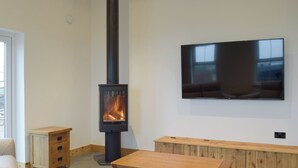 A modern living room with a wood-burning stove, a flat-screen TV mounted on the wall, and a wooden bench. - 2 bedroom accommodation in Glandwr, near Narbeth (Glandwr, near Narbeth)