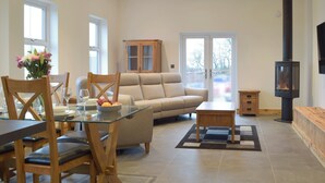 A modern living room with a glass dining table, wooden chairs, a beige sofa, and a black fireplace. - 2 bedroom accommodation in Glandwr, near Narbeth (Glandwr, near Narbeth)