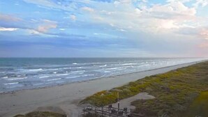 A coastal view with a beach, ocean, and a grassy area with some structures.