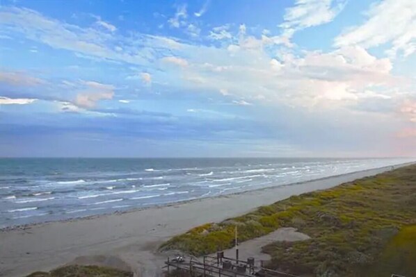 A coastal view with a beach, ocean, and a grassy area with some structures.