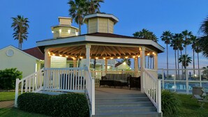 A gazebo with a covered patio, steps leading up to it, and a pool in the background.