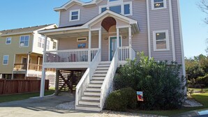 A two-story house with a front porch, a staircase leading to the entrance, and a small garden area. - OS733- 6 Bedrooms- Tiki Bar- Private Pool and Hot Tub! (Corolla)