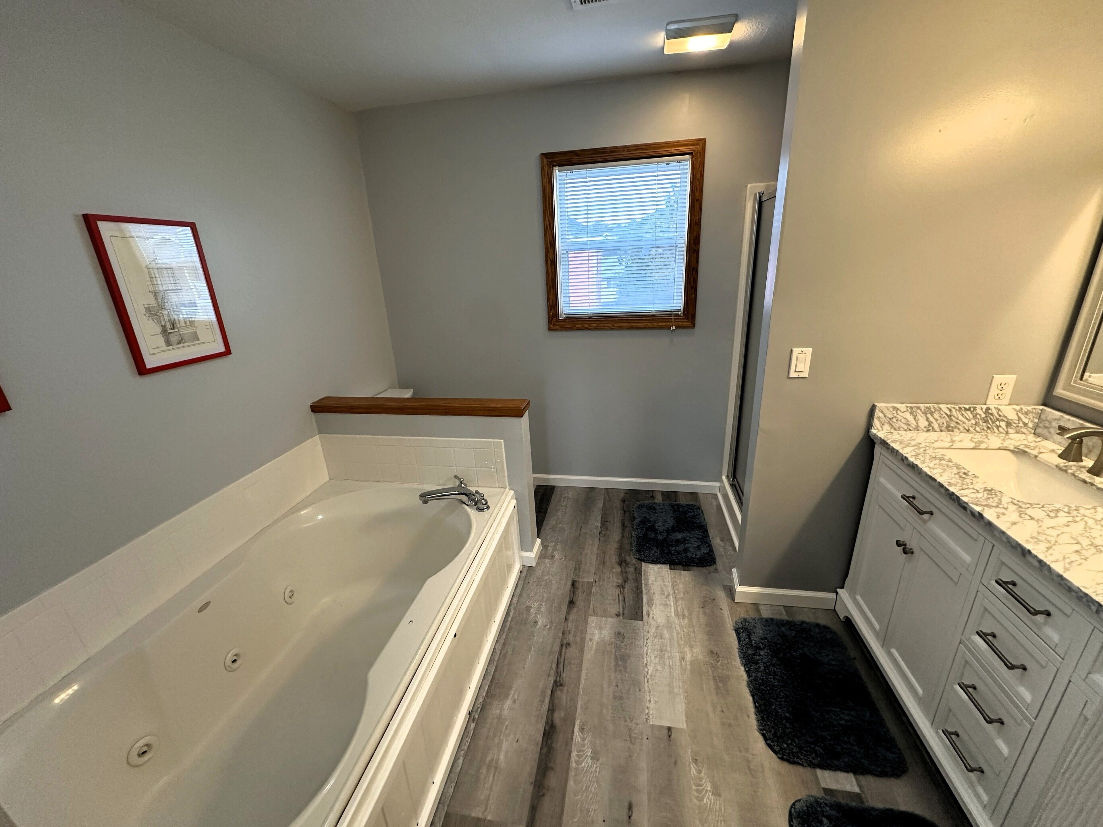 Une salle de bain avec une baignoire, un meuble-lavabo et une fenêtre avec des stores.