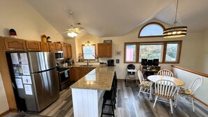 A spacious kitchen with a central island, wooden cabinets, stainless steel appliances, and a dining area with white chairs. - OS733- 6 Bedrooms- Tiki Bar- Private Pool and Hot Tub! (Corolla)