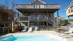 A two-story building with a balcony, a swimming pool, and outdoor seating. - OS733- 6 Bedrooms- Tiki Bar- Private Pool and Hot Tub! (Corolla)
