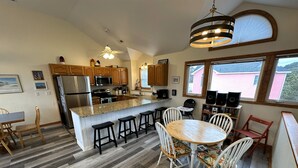 A modern kitchen with a central island, wooden bar stools, and a dining table with chairs. - OS733- 6 Bedrooms- Tiki Bar- Private Pool and Hot Tub! (Corolla)