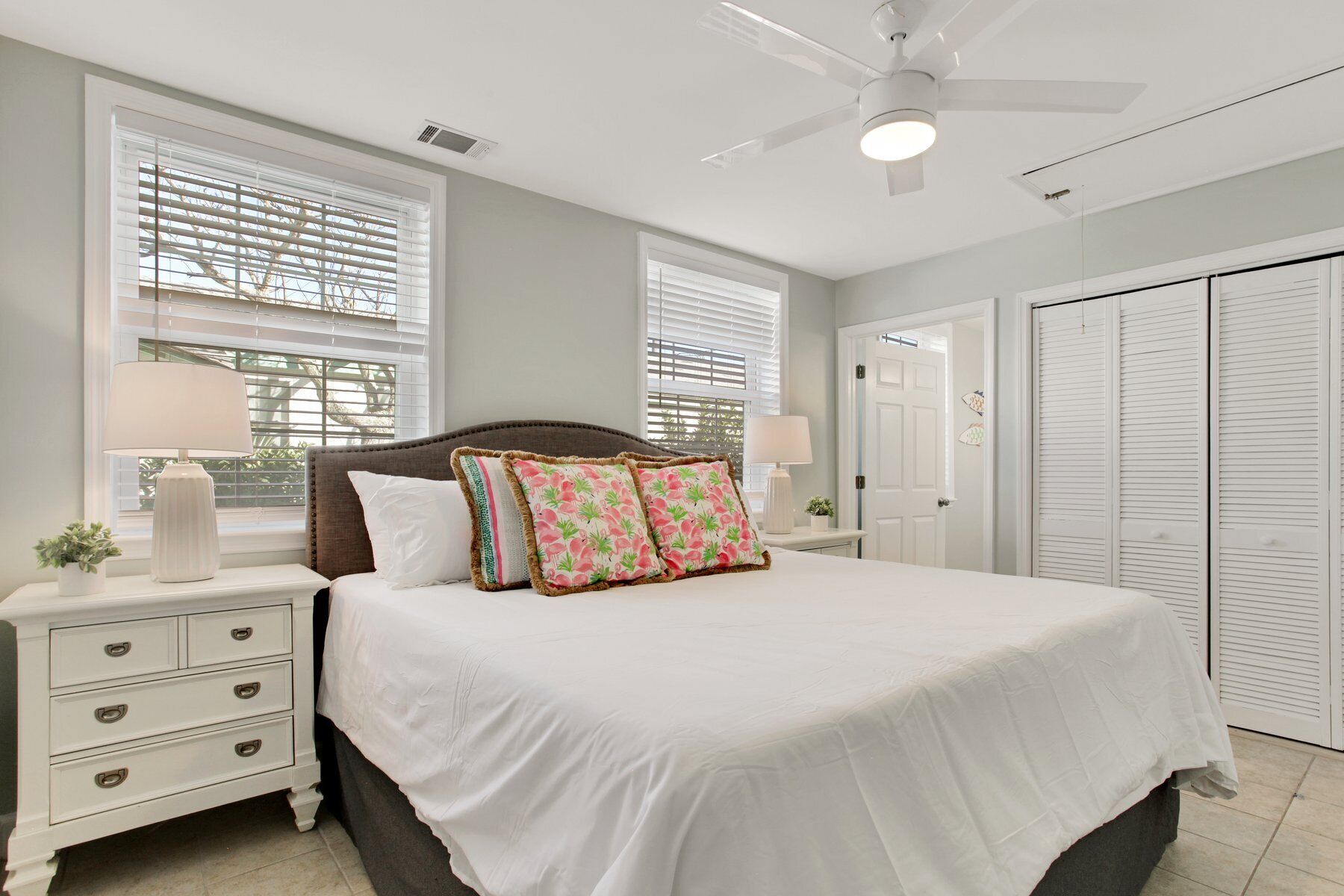 Quarto com uma cama grande, duas mesas de cabeceira com luminárias, um ventilador de teto e um guarda-roupa com portas deslizantes.