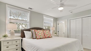 Une chambre à coucher avec un grand lit, deux tables de chevet avec des lampes, un ventilateur de plafond et un placard avec des portes coulissantes.